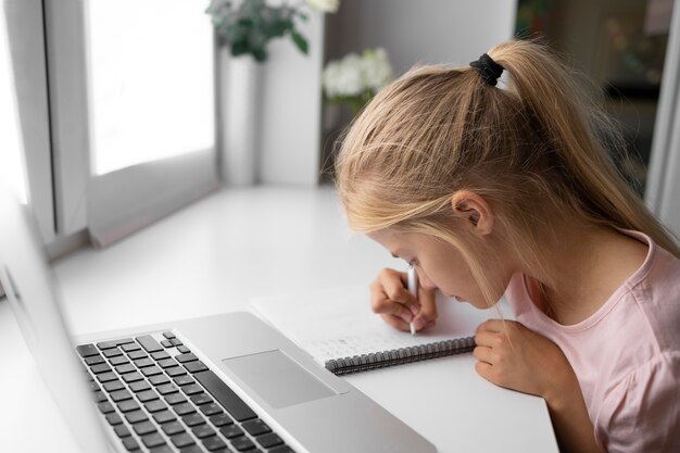 Niña haciendo los deberes en casa con laptop y notebook