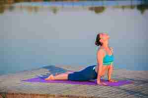 Foto gratuita niña haciendo ejercicios de yoga en la orilla del río al atardecer