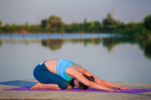 Foto gratuita niña haciendo ejercicios de yoga en la orilla del río al atardecer