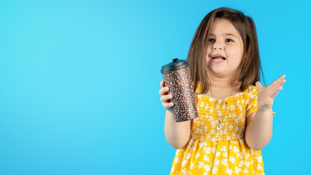 Una niña hermosa y sonriente con una cara graciosa con un vestido amarillo a rayas posando sobre un fondo azul en el estudio