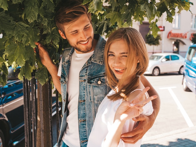 Niña hermosa sonriente y su novio guapo posando en la calle cerca del árbol.