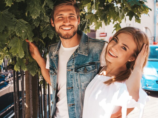 Niña hermosa sonriente y su novio guapo posando en la calle cerca del árbol.