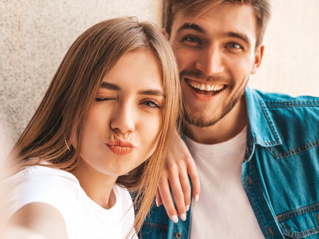 Niña hermosa sonriente y su novio guapo en ropa casual de verano. Familia feliz tomando selfie autorretrato de sí mismos en la cámara del teléfono inteligente. Divirtiéndose y haciendo cara de pato