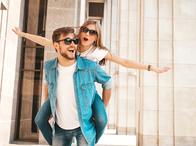 Niña hermosa sonriente y su novio guapo en ropa casual de verano. Hombre con su novia en la espalda y ella levantando las manos.