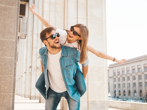 Niña hermosa sonriente y su novio guapo en ropa casual de verano. Hombre con su novia en la espalda y ella levantando las manos.