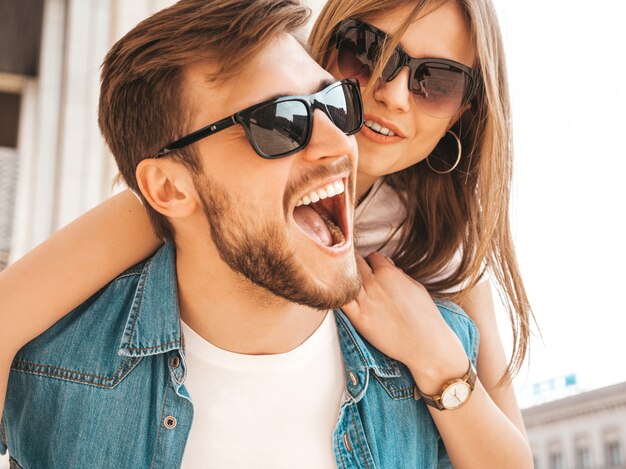 Niña hermosa sonriente y su novio guapo en ropa casual de verano. Hombre con su novia en la espalda y ella levantando las manos.