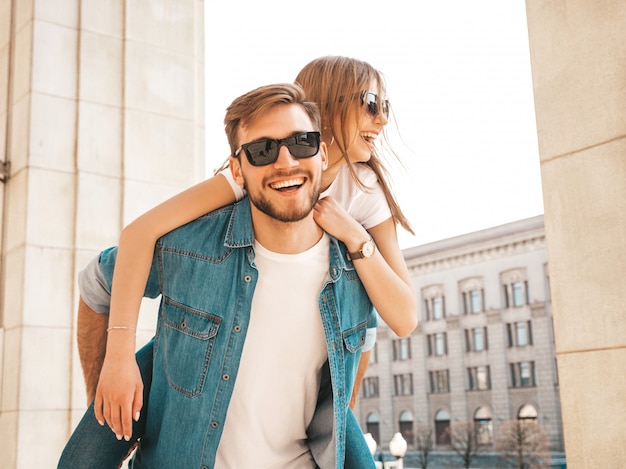 Niña hermosa sonriente y su novio guapo en ropa casual de verano. Hombre con su novia en la espalda y ella levantando las manos.