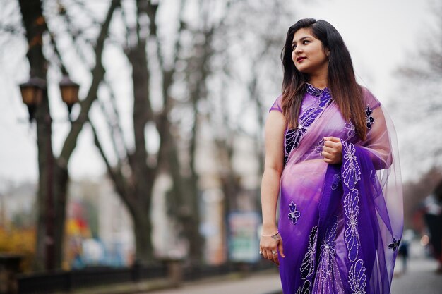 Niña hindú india en sari violeta tradicional posada en la calle