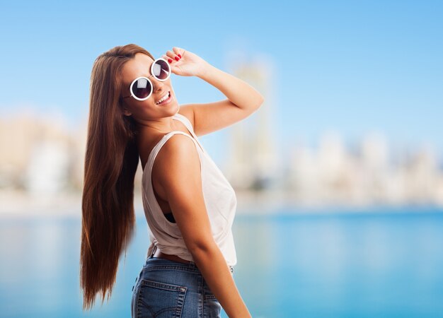 niña hispana feliz en gafas de sol posando en contra de la ciudad