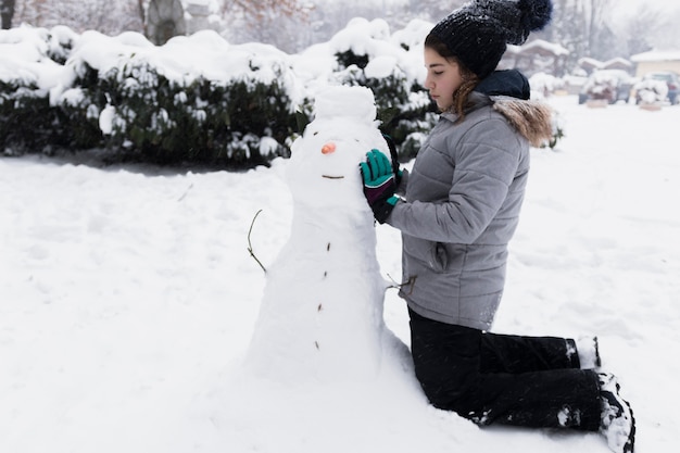 Foto gratuita niña inocente tocando muñeco de nieve en invierno