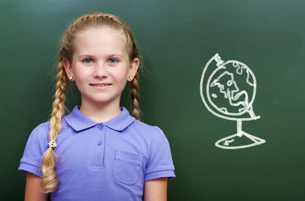 Niña inteligente con un globo terráqueo en la pizarra