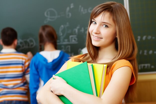 Niña inteligente sujetando libros en el aula