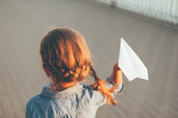 Niña jugando con avión de papel de juguete