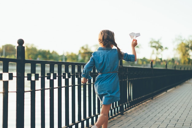 Niña jugando, corriendo con avión de papel de juguete