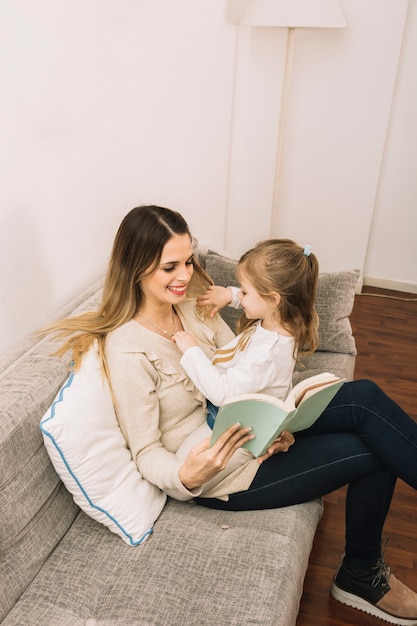 Niña jugando con el pelo y accesorios de lectura de mamá