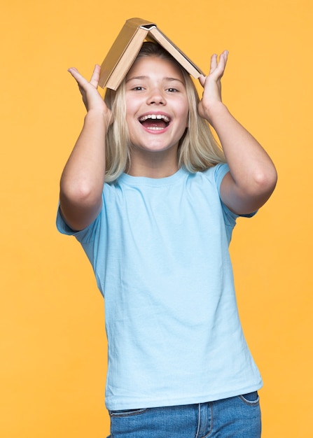 Foto gratuita niña juguetona con libro en la cabeza