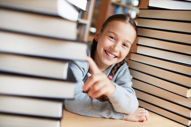 Niña juguetona con libros en la biblioteca