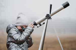 Foto gratuita niña de lado usando un telescopio