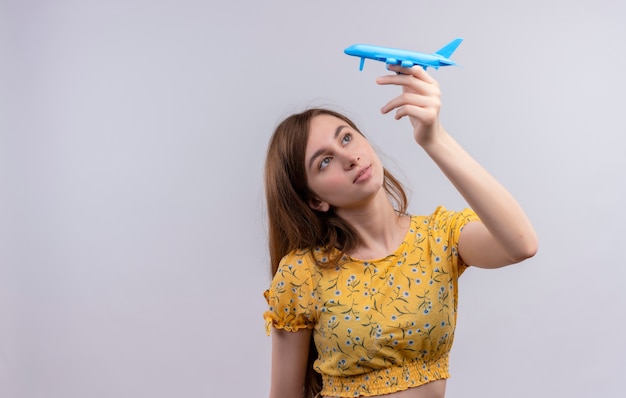 Foto gratuita niña levantando modelo de avión y mirándolo en una pared blanca aislada con espacio de copia