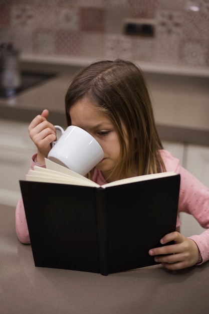 Foto gratuita niña leyendo libro y bebiendo