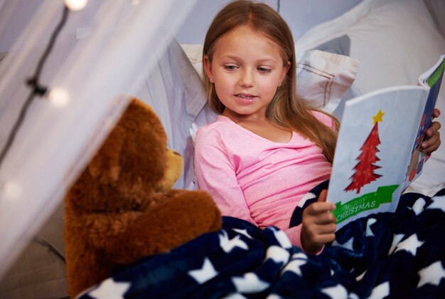 Niña leyendo un libro de cuentos con su osito de peluche