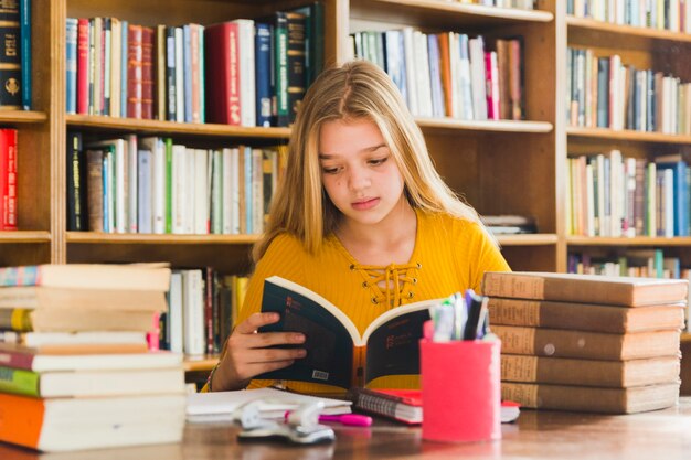 Niña leyendo un libro sentado en la biblioteca