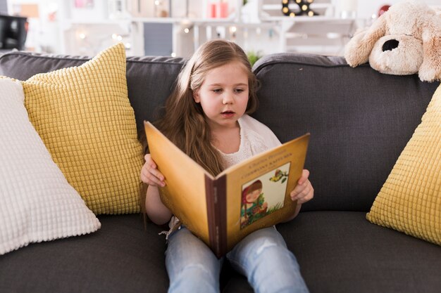 Niña leyendo libro en sofá