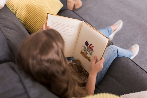 Niña leyendo un libro en sofá