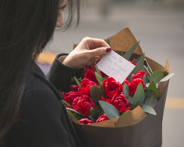 Niña leyendo una nota puesta en un ramo de tulipanes rojos