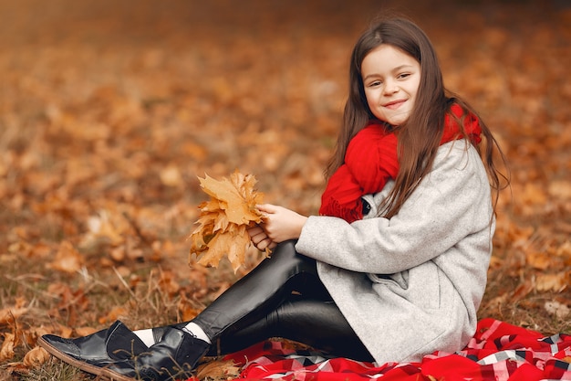 Niña linda en un abrigo gris jugando en un parque de otoño