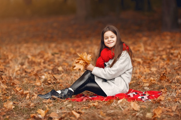 Niña linda en un abrigo gris jugando en un parque de otoño