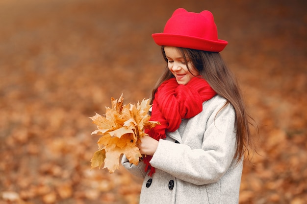 Niña linda en un abrigo gris jugando en un parque de otoño