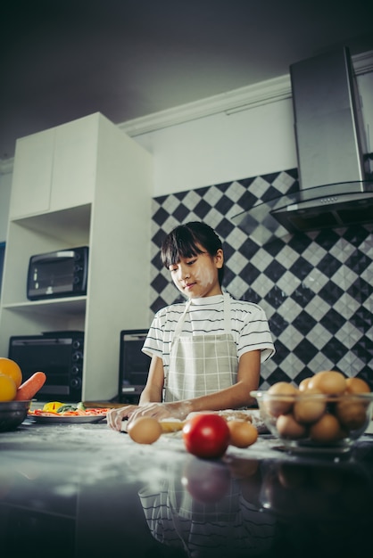 La niña linda amasa la pasta de la harina que se prepara para hace la pizza. Concepto de cocina