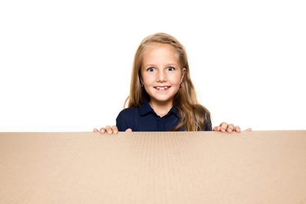 Niña linda y asombrada abriendo el paquete postal más grande. Modelo de mujer joven emocionada en la parte superior de la caja de cartón mirando hacia adentro.