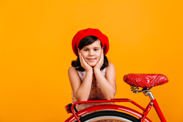 Niña linda en boina francesa posando con bicicleta. niño sonriente aislado en amarillo.