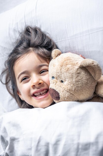 Niña linda en la cama con un oso de peluche temprano en la mañana