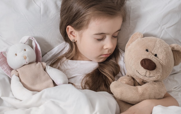 Niña linda en la cama con peluche.