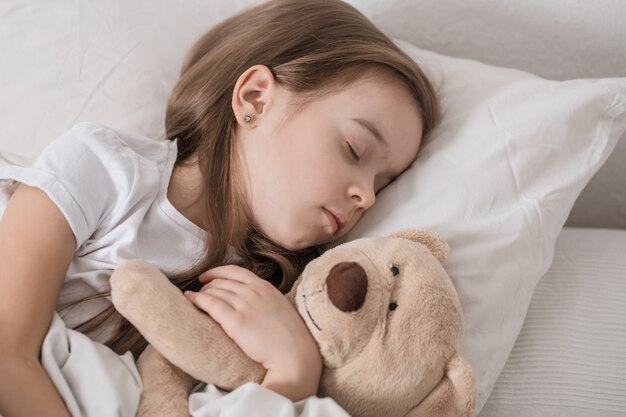 Niña linda en la cama con peluche.