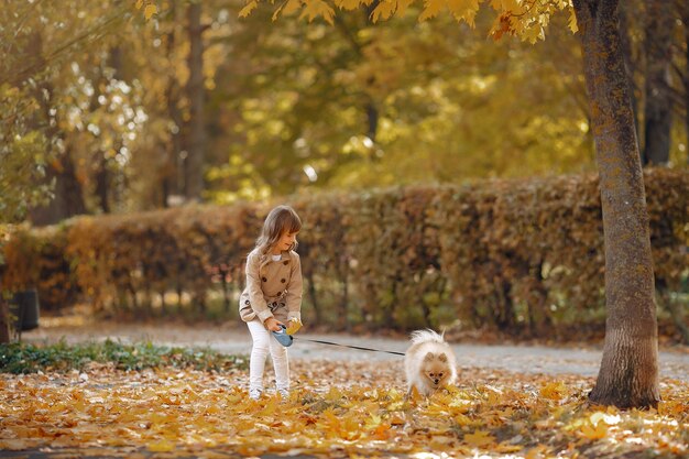 Niña linda camina en un parque de otoño con un perro