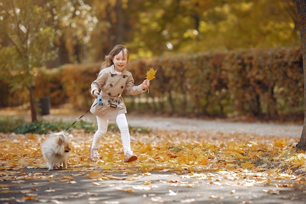 Niña linda camina en un parque de otoño con un perro