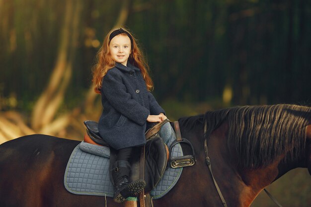 Niña linda en un campo de otoño con caballo