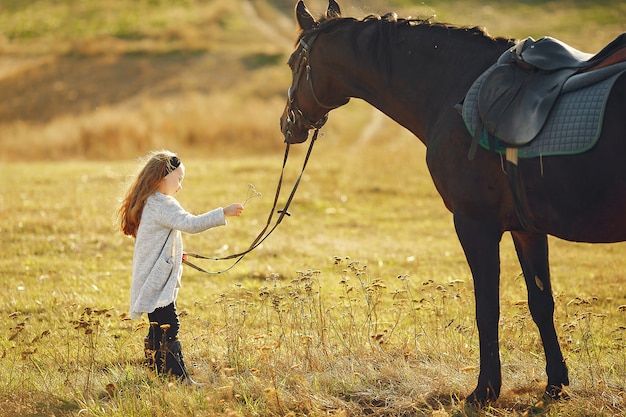 Niña linda en un campo de otoño con caballo