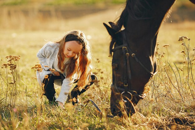 Niña linda en un campo de otoño con caballo