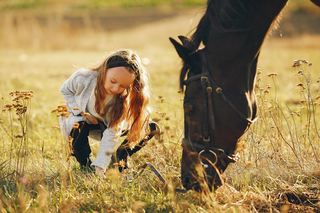 Niña linda en un campo de otoño con caballo