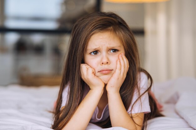 Niña linda con una cara triste acostada en la cama