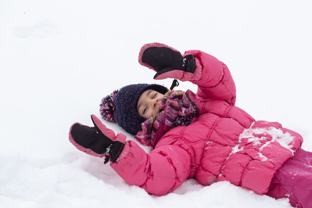 Una niña linda con una chaqueta rosa y un sombrero está jugando en la nieve. Concepto de entretenimiento infantil de invierno.