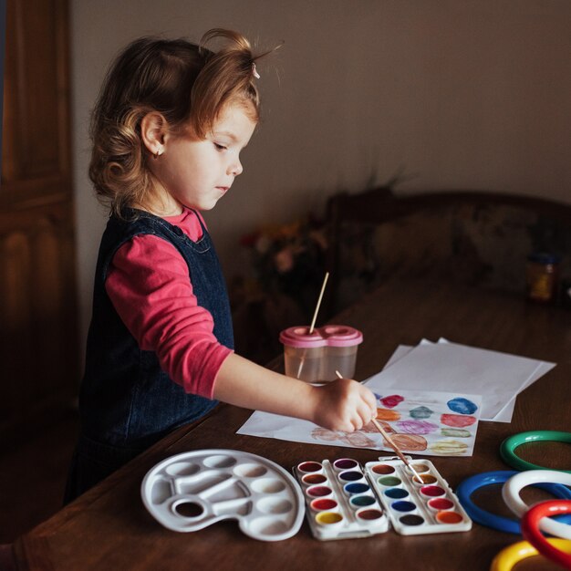 Niña linda dibuja un círculo de pinturas de colores