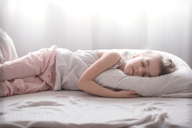 Niña linda duerme dulcemente en una acogedora cama blanca, el concepto de descanso y sueño de los niños
