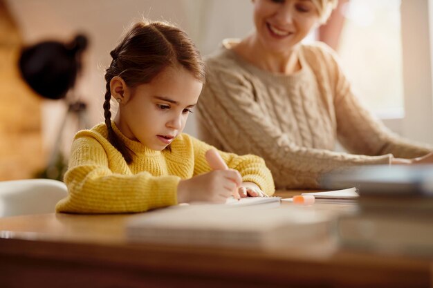 Niña linda escribiendo mientras su madre trabaja a su lado en casa