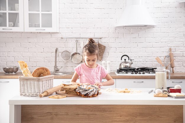 niña linda está cocinando pasteles caseros en la cocina.